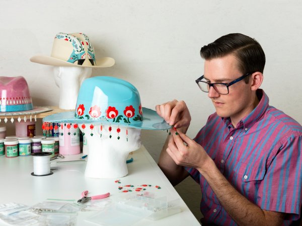 artist working on a decorated hat at a table in a studio