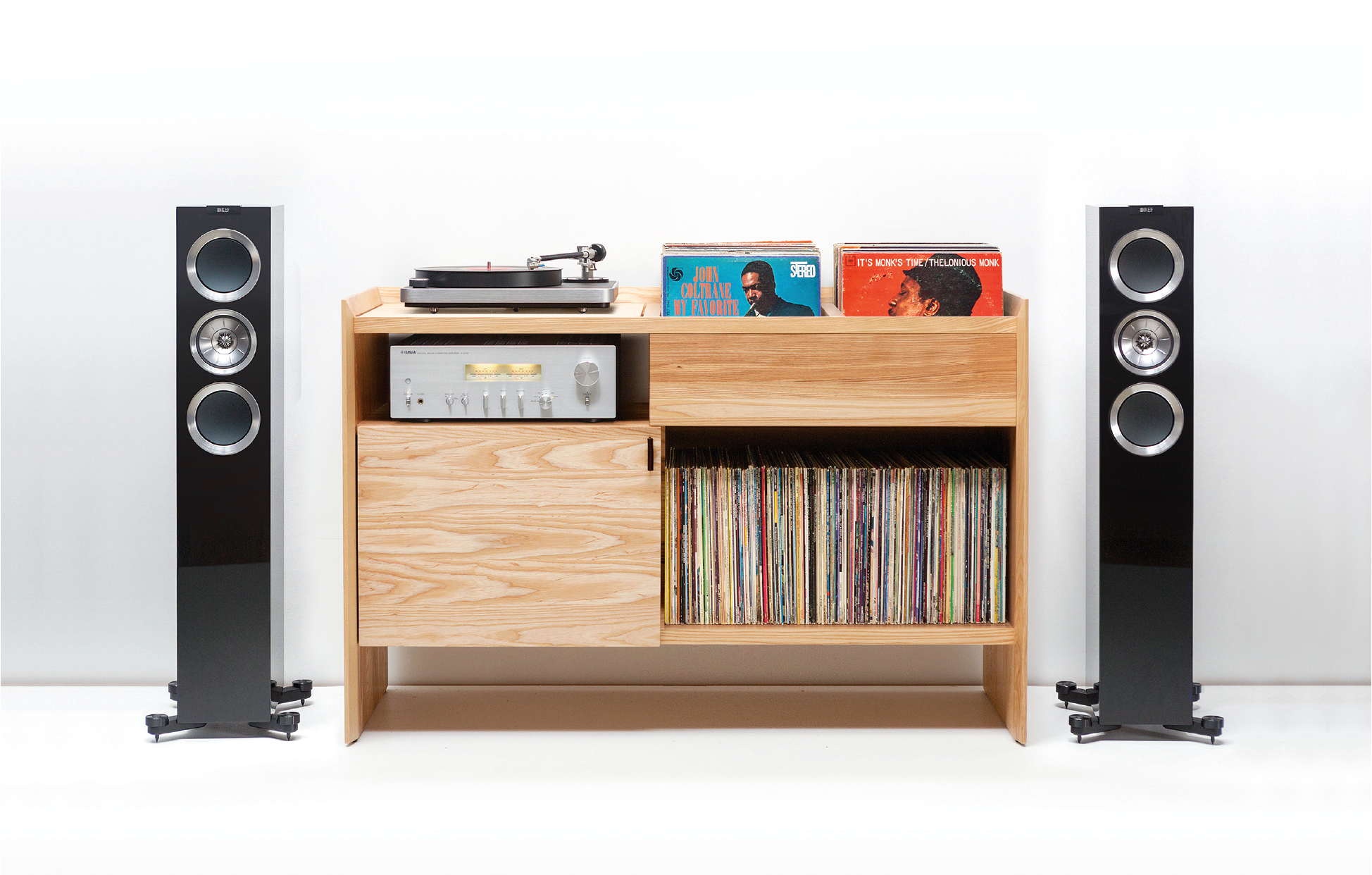 The 52-inch Unison model from Symbol Audio in natural ash, 34 x 52 x 18 in., holds stereo equipment behind a swinging door and up to 420 LPs. It features a vibration-isolated turntable platform and flip bin–style record storage.