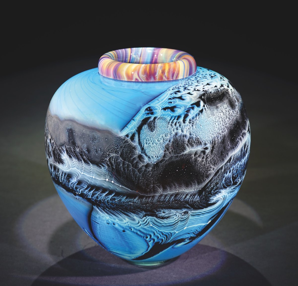 Vase with light blues, dark greys, blacks, leading to multiple colors around the top.