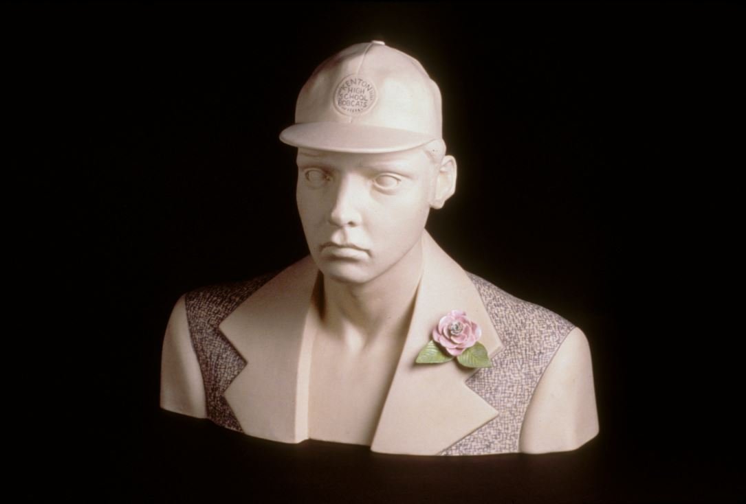 Ceramic bust of a boy with a cap and flower on lapel.