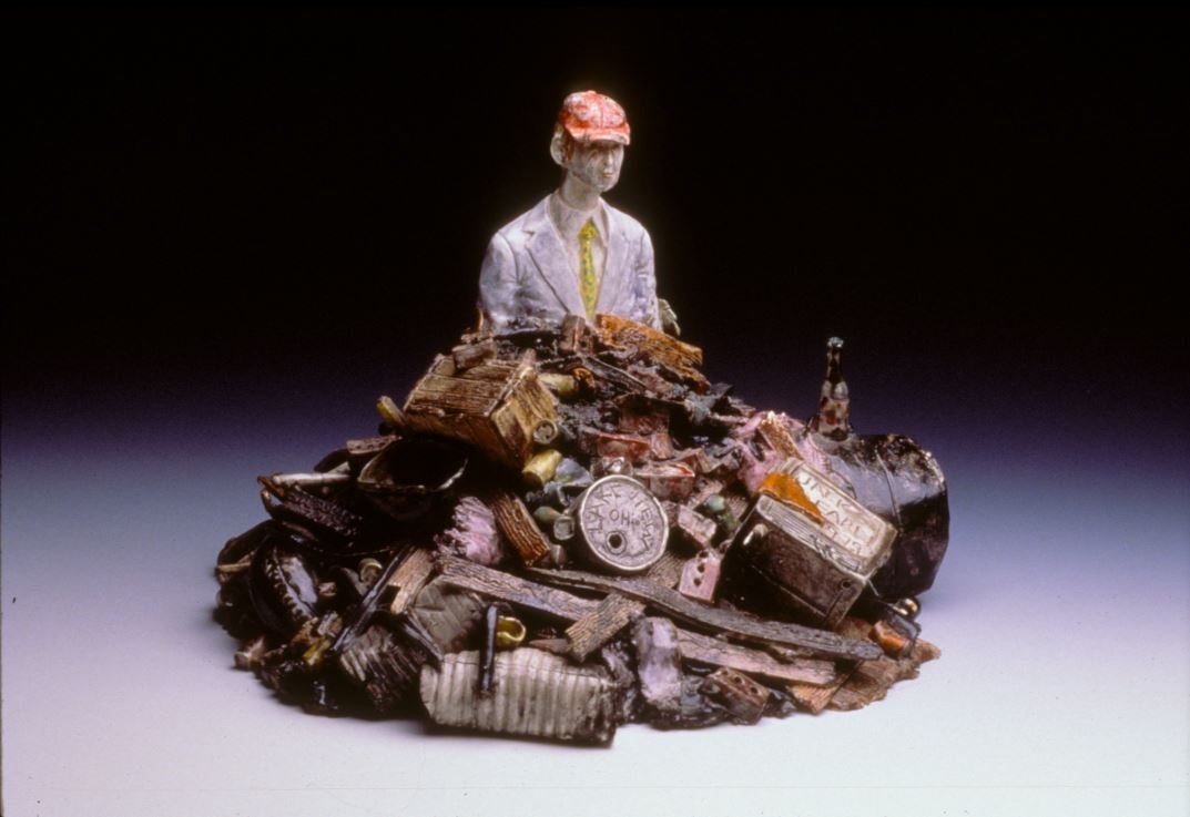 Ceramic sculpture of the torso of a man sticking out from a pile of trash.