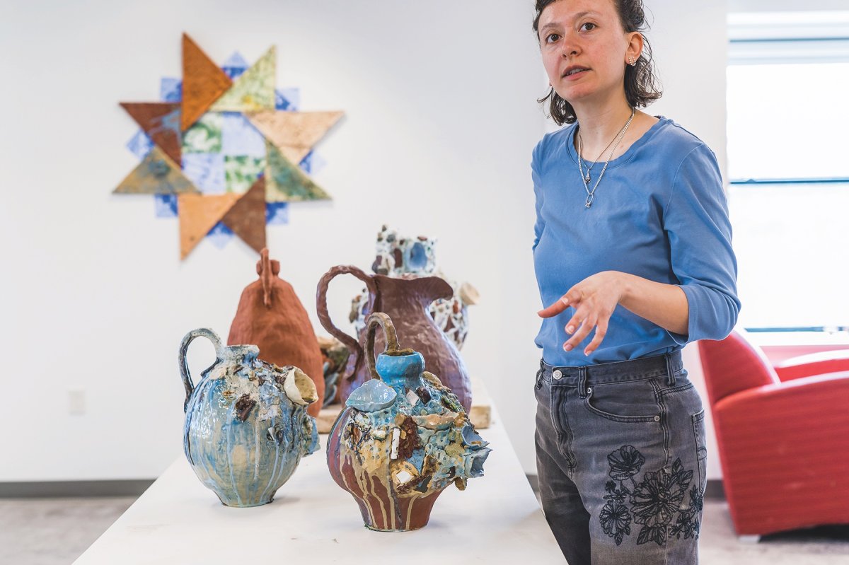 Downing standing with her foraged ceramic art vessels and wall hangings.
