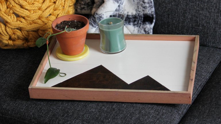 Wooden try with black and white mountain pattern on a couch with plant and other objects
