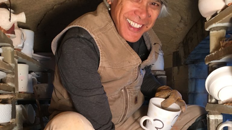 portrait of ceramist conrad calimpong crouched inside a kiln with unfired ceramics