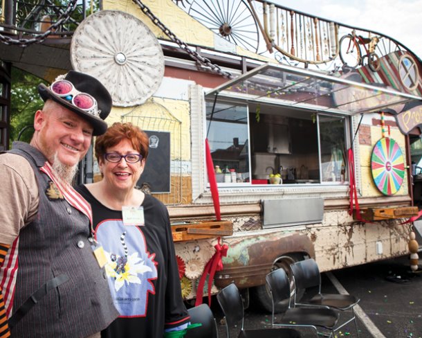 Two people one wearing circus inspired clothing posing in front of a circus-decorated food truck
