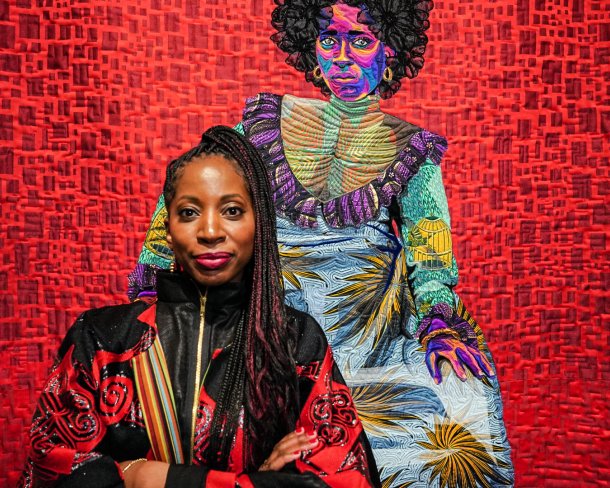 artist in red and black shirt posing in front of quilt depicting woman in vibrant colors over red backdrop