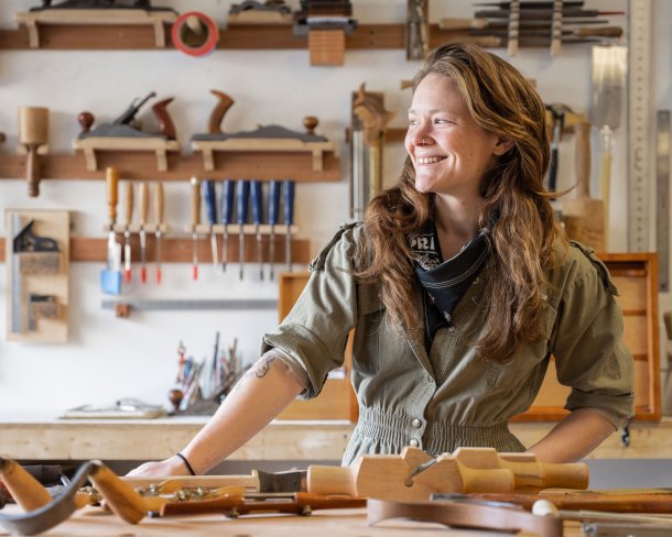 woodworker in studio looking away from camera and smiling while standing at bench with tools