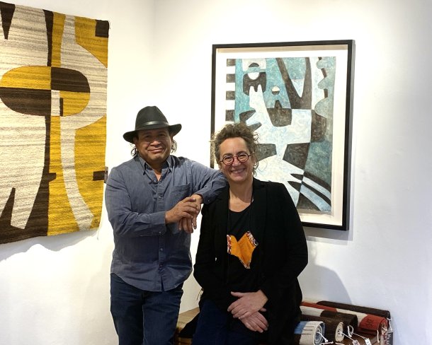 two artists posing in their studio with weavings and symbolist paintings hanging on the walls