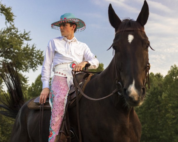 portrait of shae bishop on horseback wearing ornate teal blue cowboy hat white shirt and ornate chaps made from pink and blue ceramic tiles