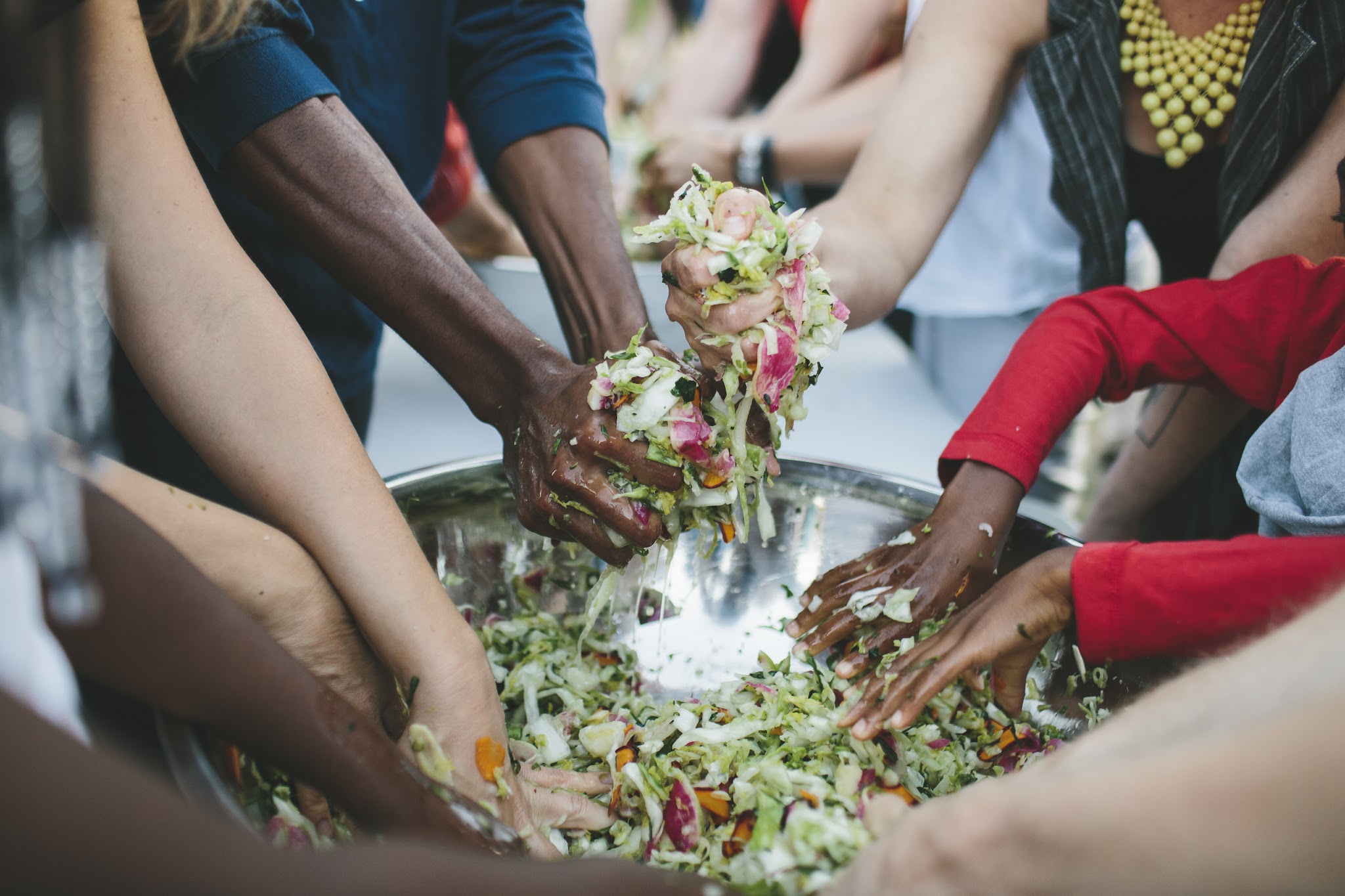 Diverse hands mixing cabbage in a large bowl