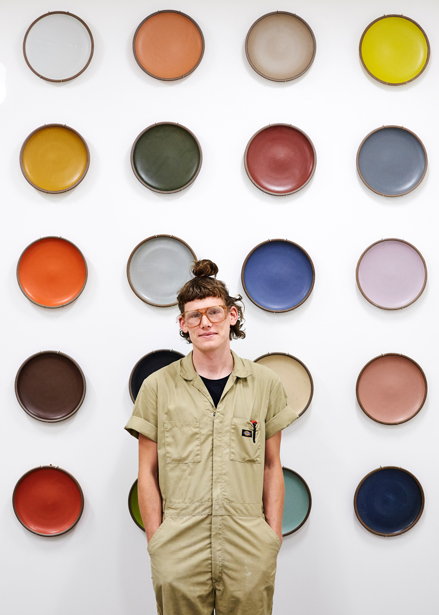 East Fork Pottery Kiln Lead Kyle Crowder standing in front of a wall of ceramic wares