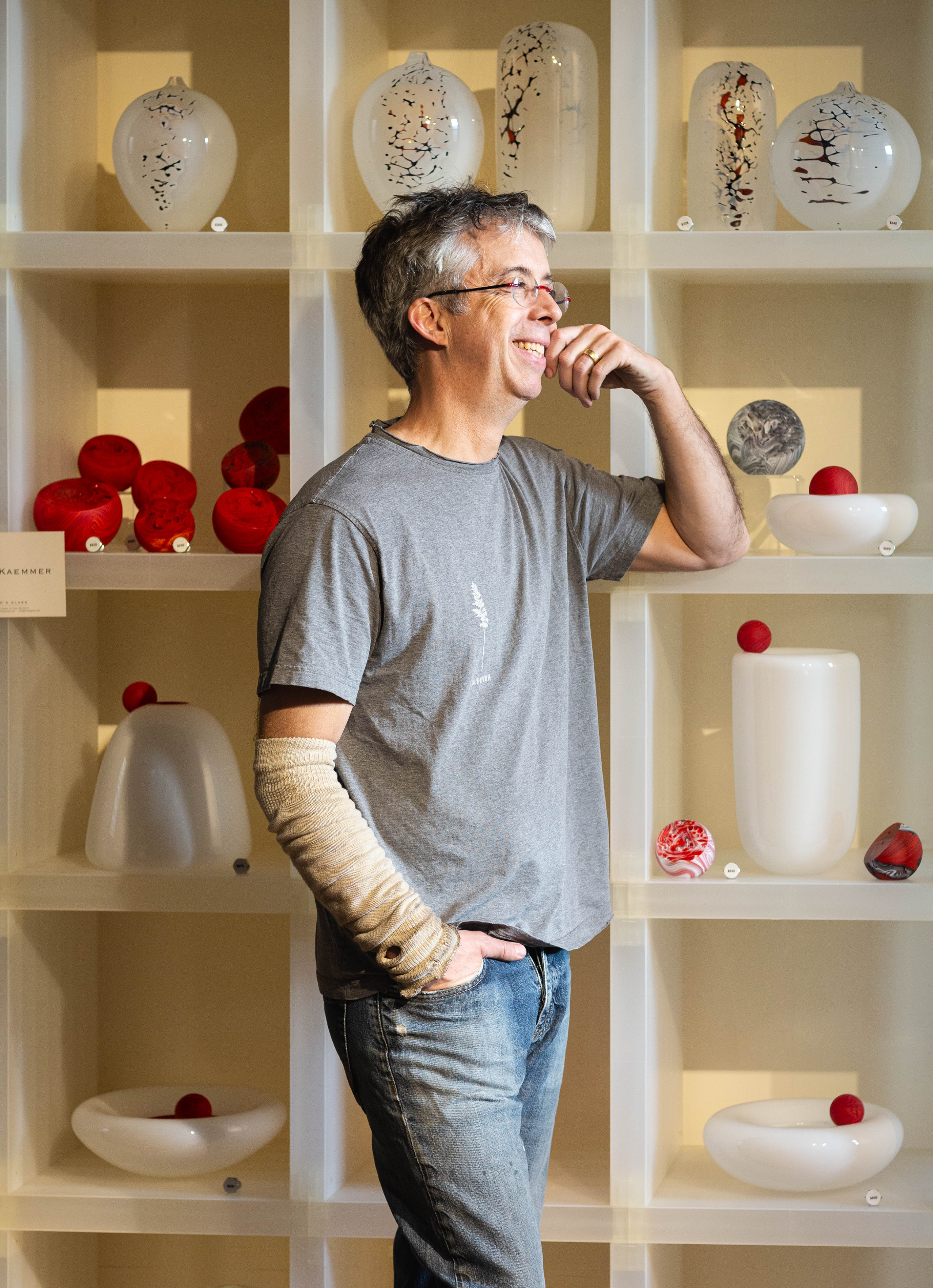 Glass artist Fred Kaemmer stands before a shelf of finished work in his studio. Photo by Dina Kantor.