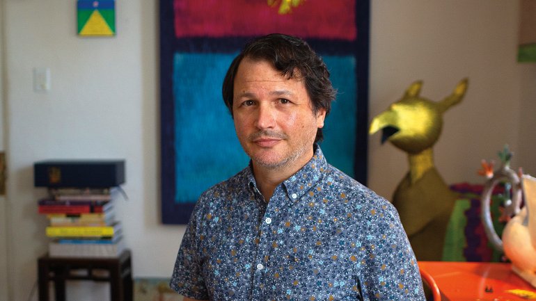 Roberto Benavidez in his studio surrounded by completed works, including Sugar Skull Piñata No.1, 2009, his very first piñata sculpture, which hangs just below the tail of one of his Bosch birds. Photo by James Bernal.