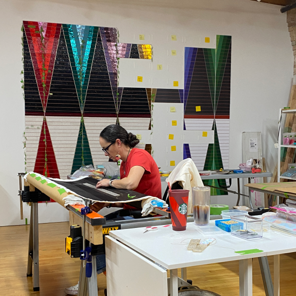 The artist works on She Gives (Quiet Strength VII), 2020, acrylic on canvas, 84 x 120 in. In the foreground is her Untitled (All the Colors), 2020, acrylic, bugle beads, thread, and synthetic sinew on canvas, 48 x 48 in. Photo courtesy of Dyani White Hawk.