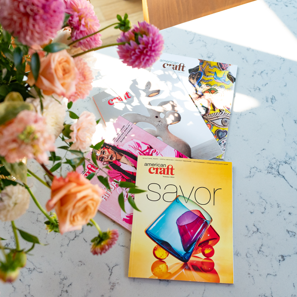 Issues of American Craft magazine spread across a marble contertop with a vase of flowers.