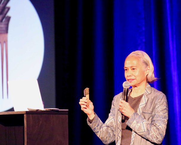 Person holding a comb and a mic presenting with a slideshow image behind them