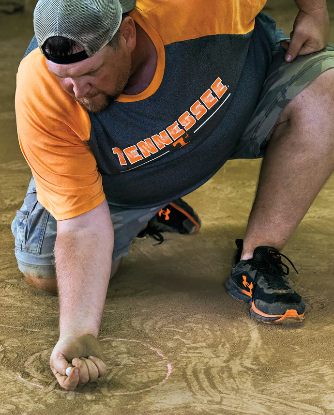 A man crouches to roll a marble.