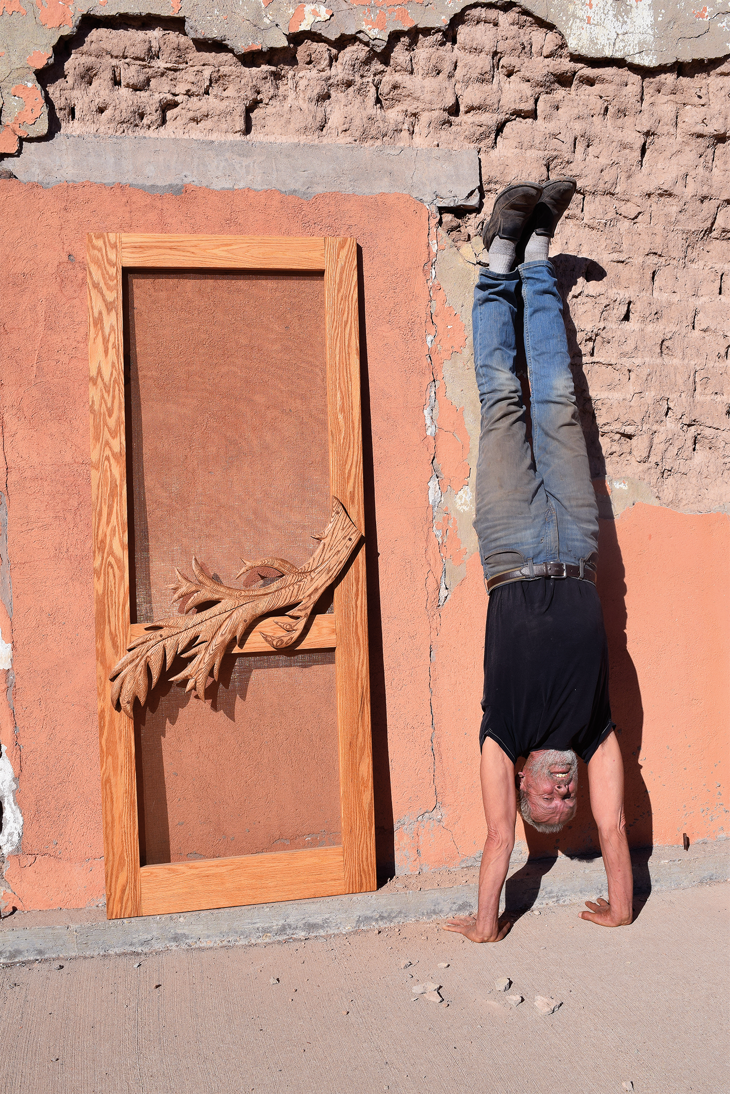 Mike Lagg does a handtand by a door with a handmade wood leaf handle.