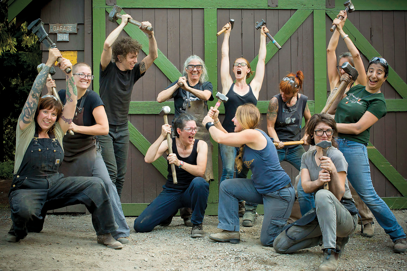 A group of women and nonbinary blacksmiths pose with mallets
