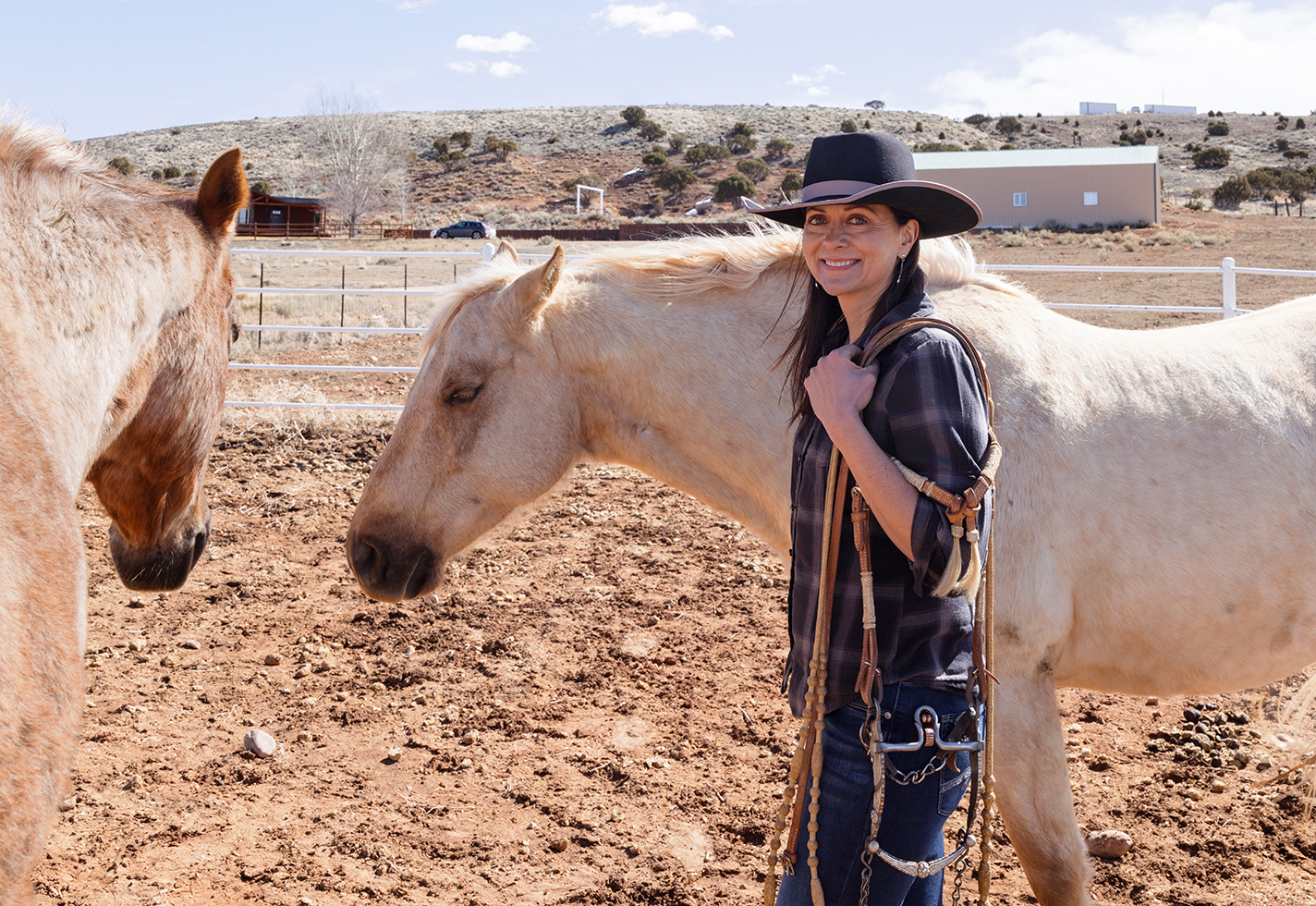 Amy Erickson on her land with two horses and a bridle she created.