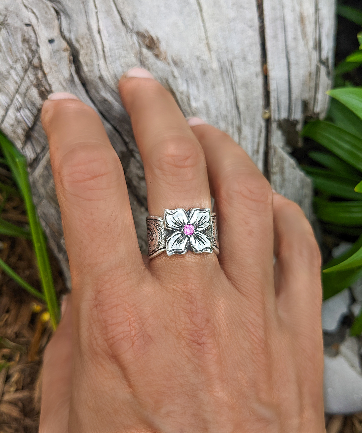 A sterling silver engraved flower ring with a pink tourmaline stone, made by Amy Erickson.