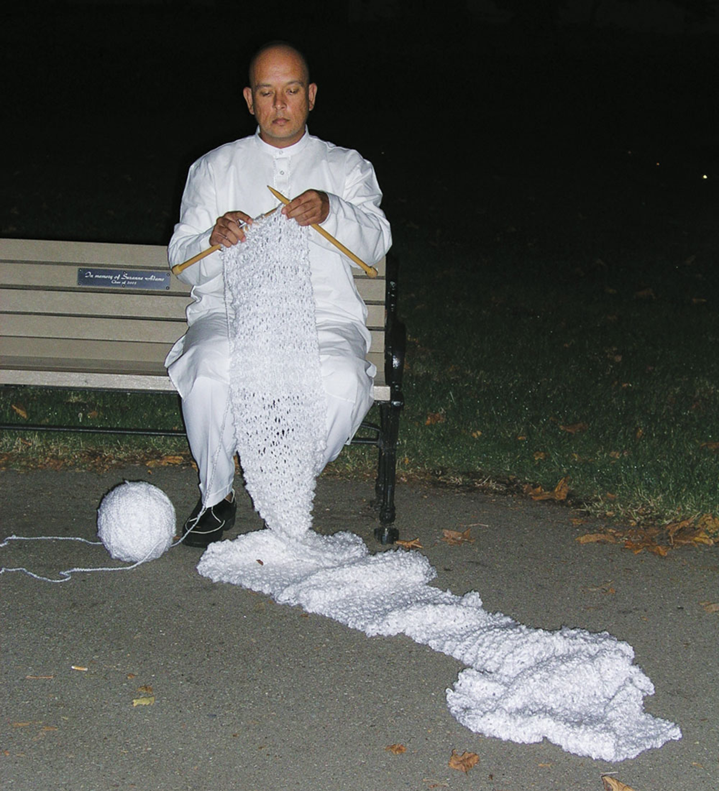 A person in a white robe knitting a long piece from white yarn.