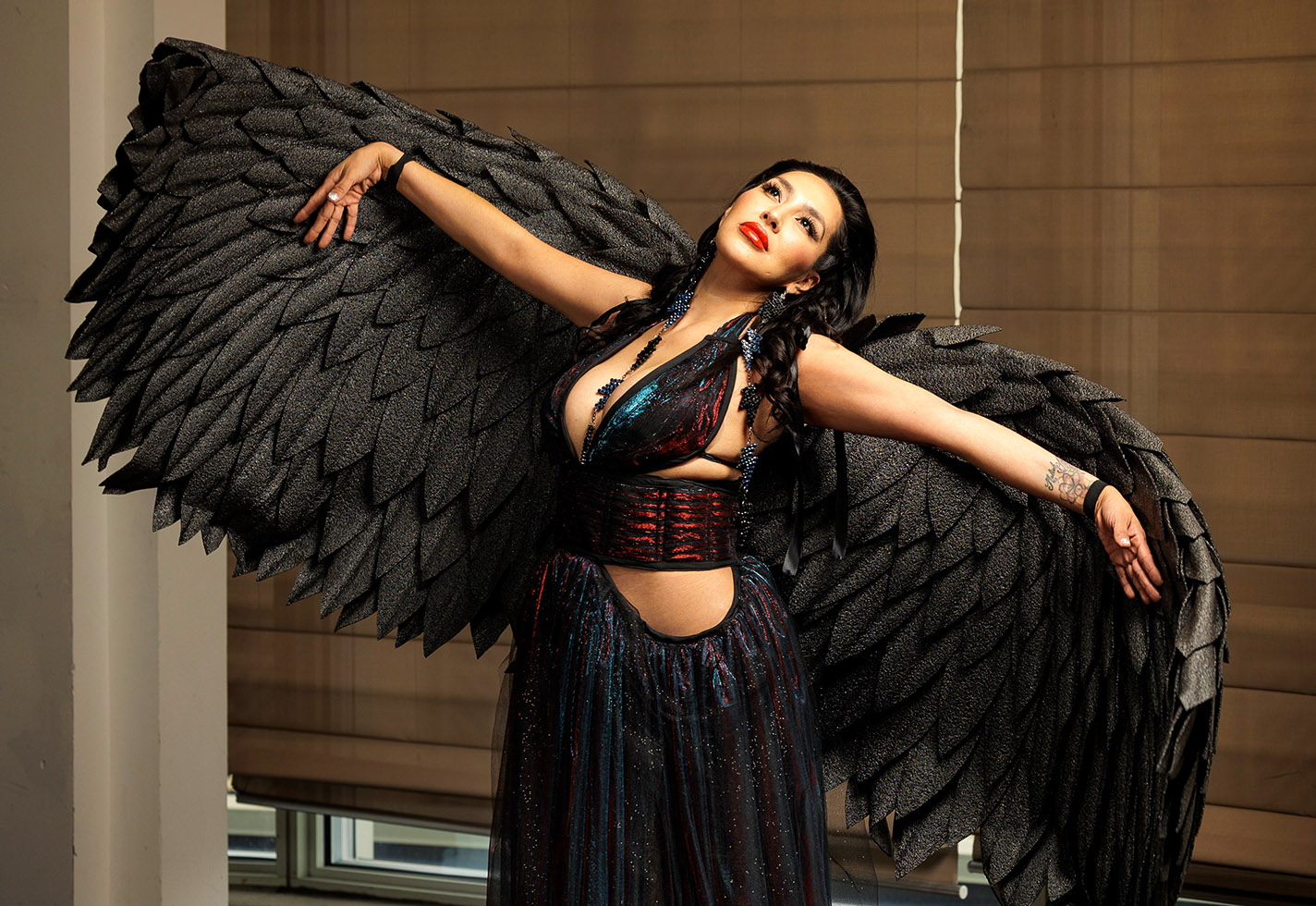 Model wears a a winged black ensemble with a cutout waist.