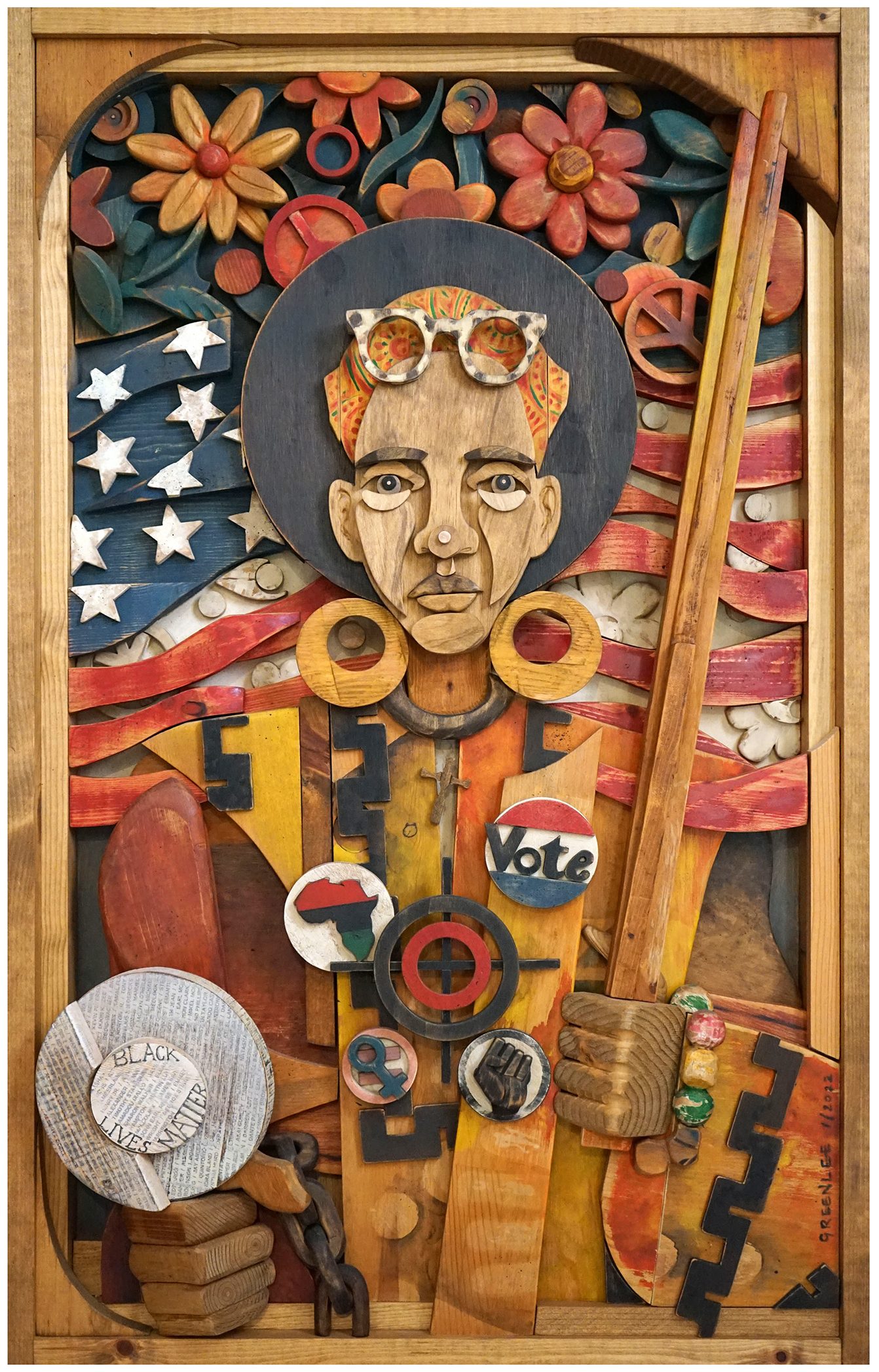 Wood collage depicting an activist holding a protect sign and wearing a variety of buttons. In the background is the American Flag and a floral motif.