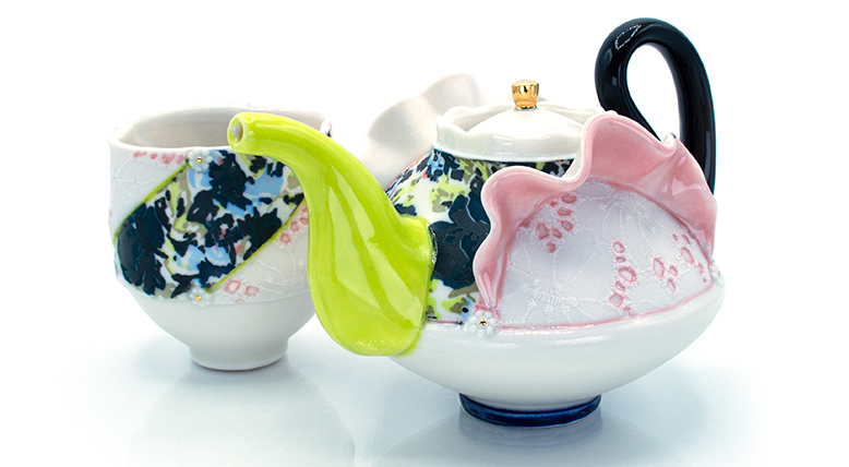 Floral-print ceramic teapot and teacup with lace inserts.