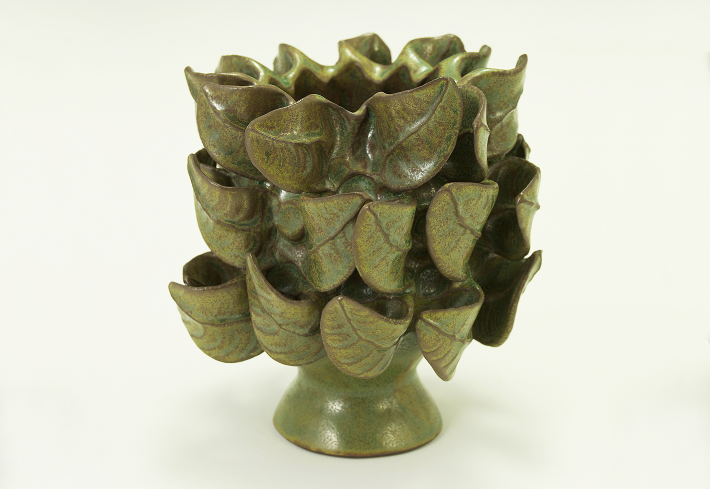 Pinch formed pedestal vase with intricate leaves and green glaze.