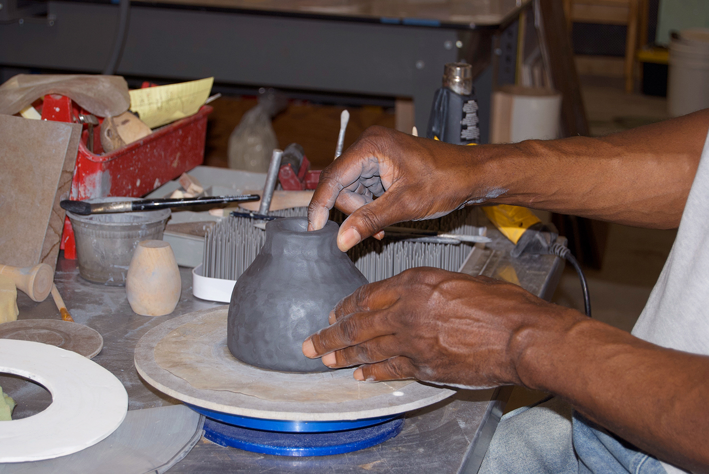 Briggs pinches black clay into the foot of a similar pedestal vase