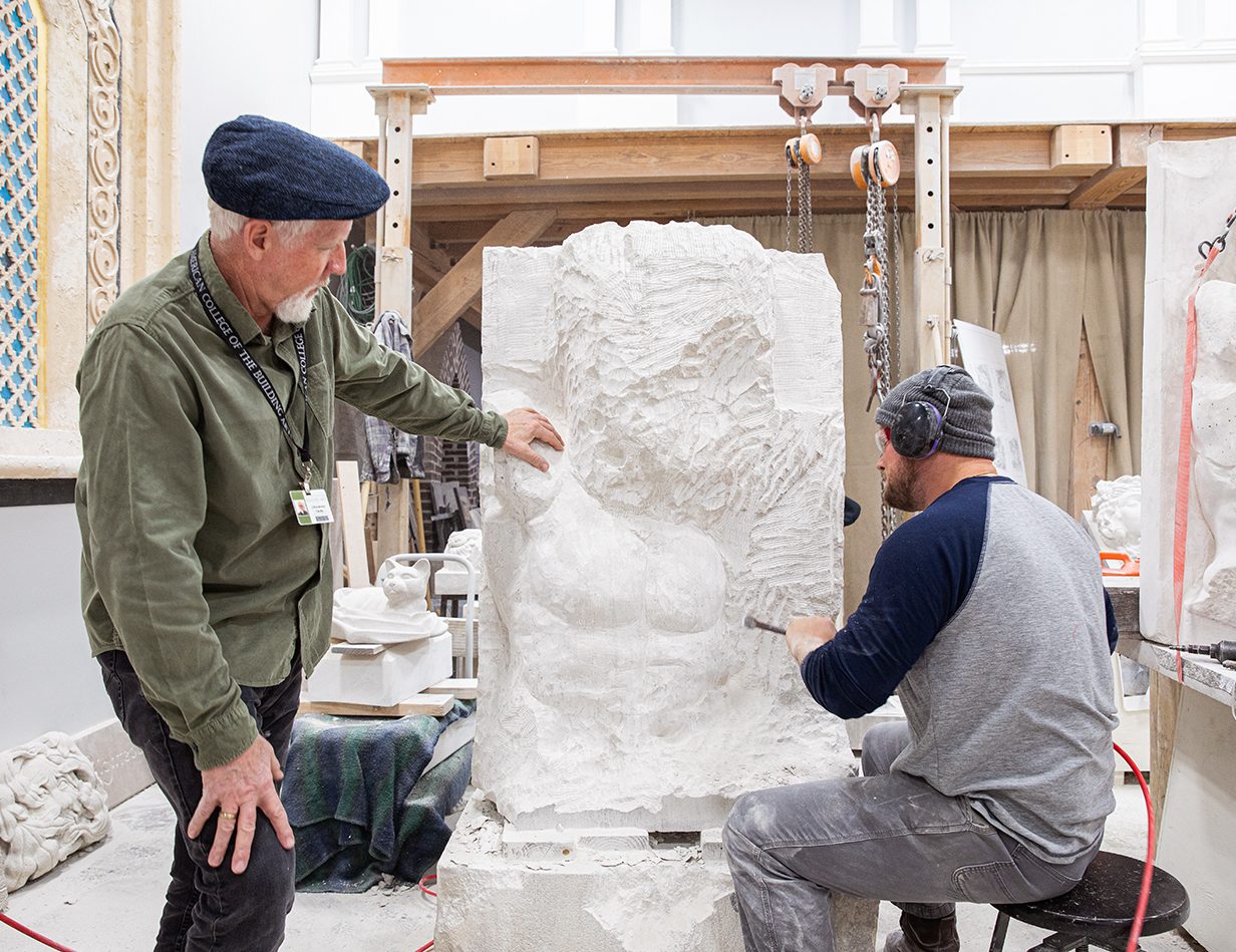 A teacher and a student work together on a stone carving