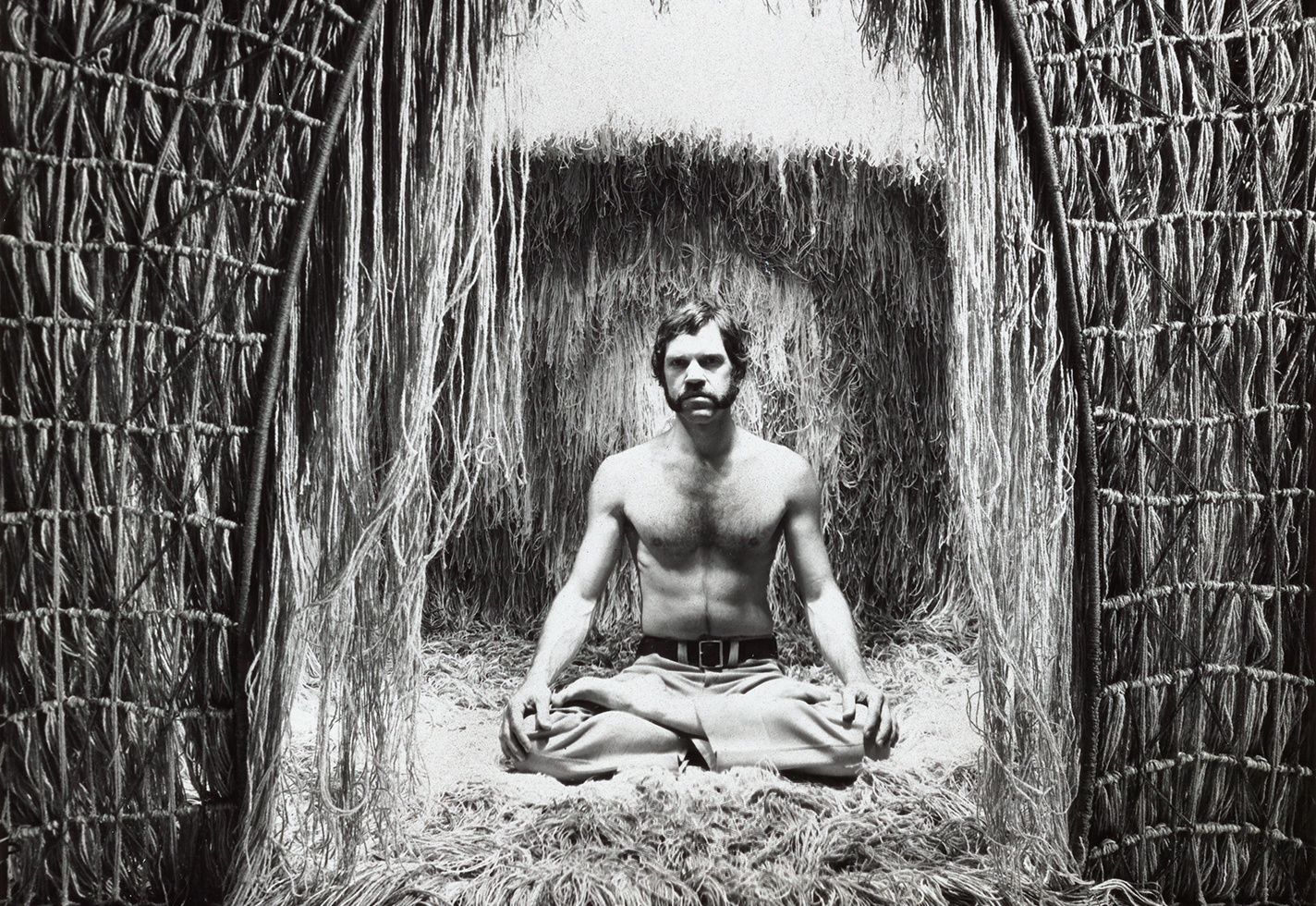 Ted Hallman seated cross-legged outside his piece.